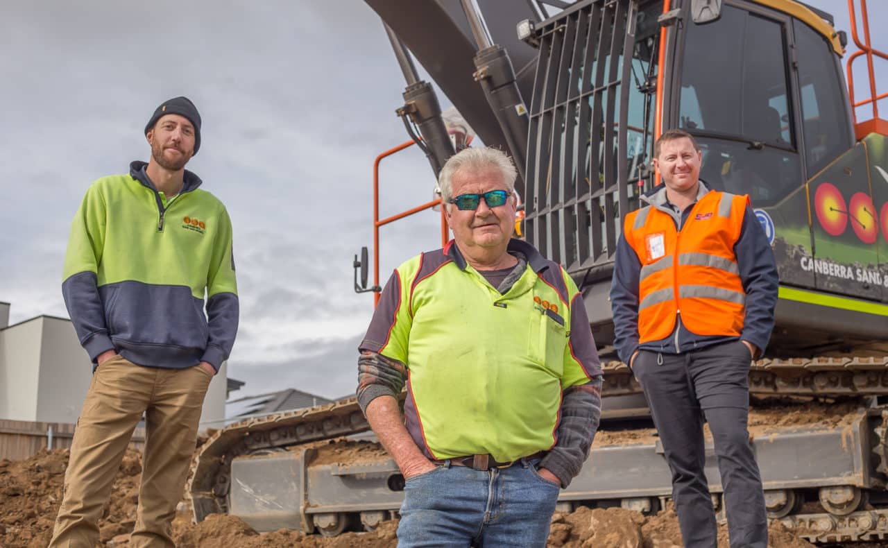 three men standing next to a piece of heavy machinery